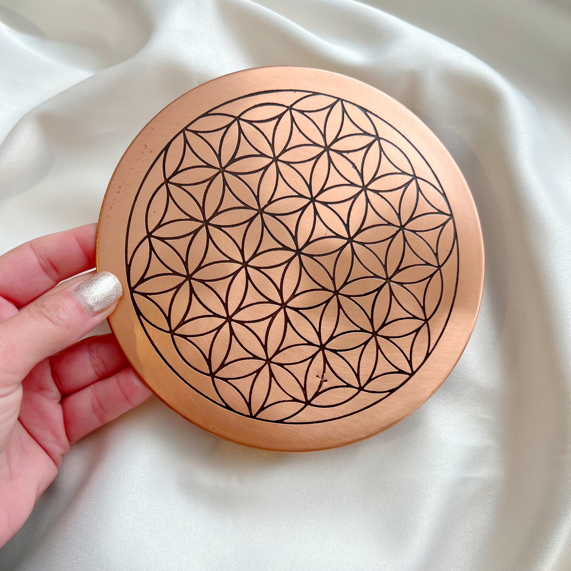 close up of copper flower of life charging plate with size comparison to hand
